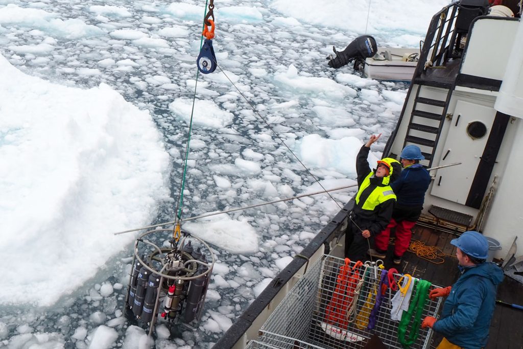 Three adults on a ship conduct scientific research in icy waters.