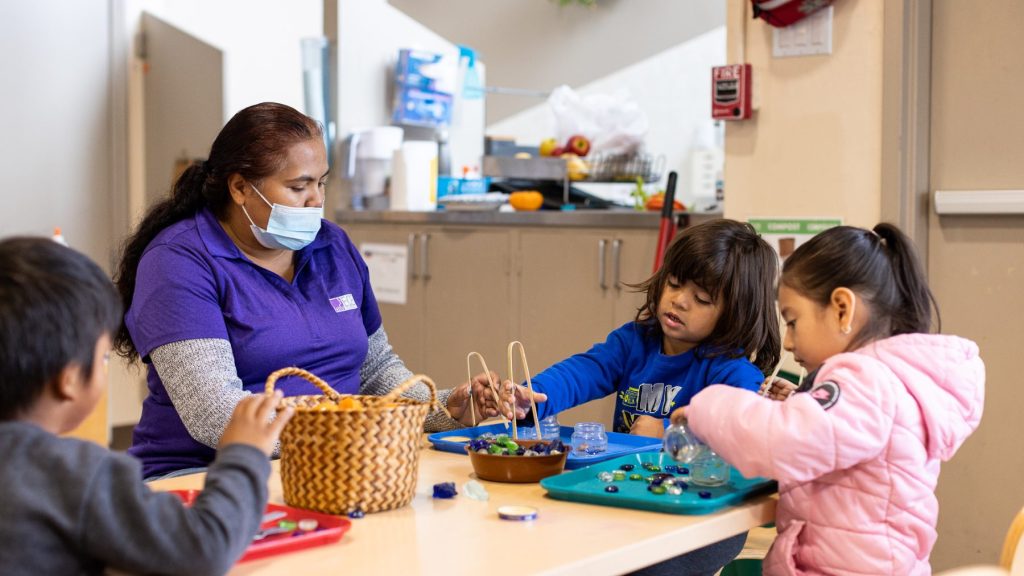 Teacher works with three young children at table.