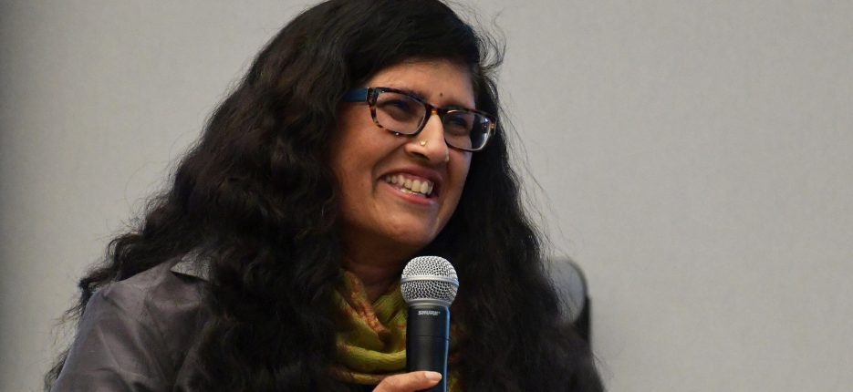 Sushma Raman smiling, holding microphone.