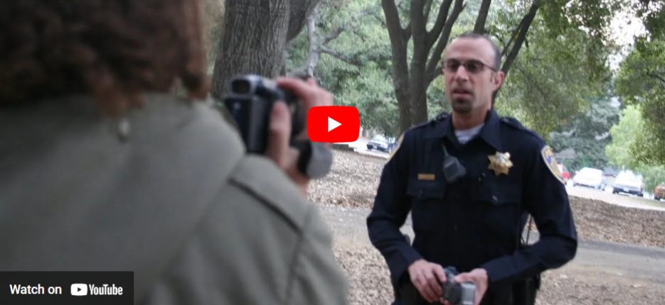 Screenshot of a person filming a police officer from WITNESS Youtube video.,