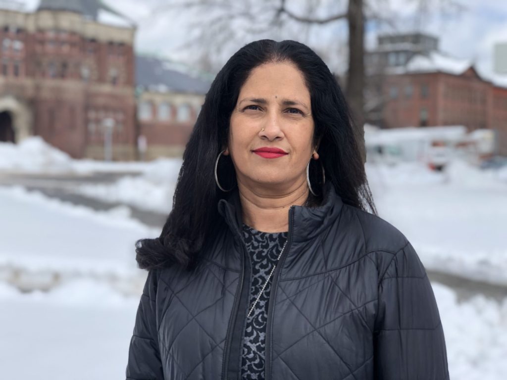 Sushma Raman smiles at camera against snowy backdrop.