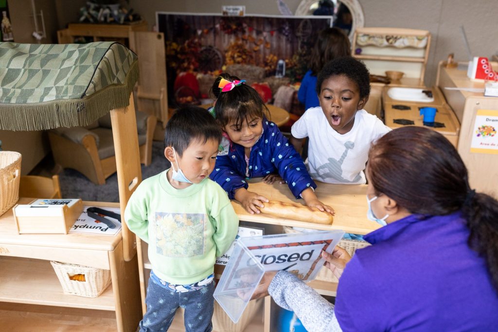 Three young children play with teacher.