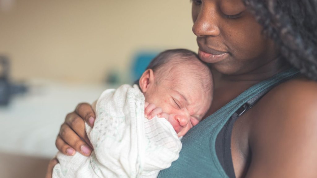 A woman holds a newborn baby to her chest.