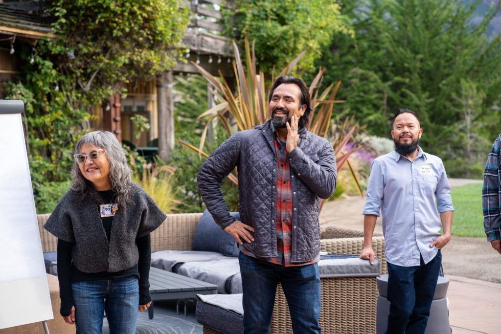 Three adults standing smiling at group.