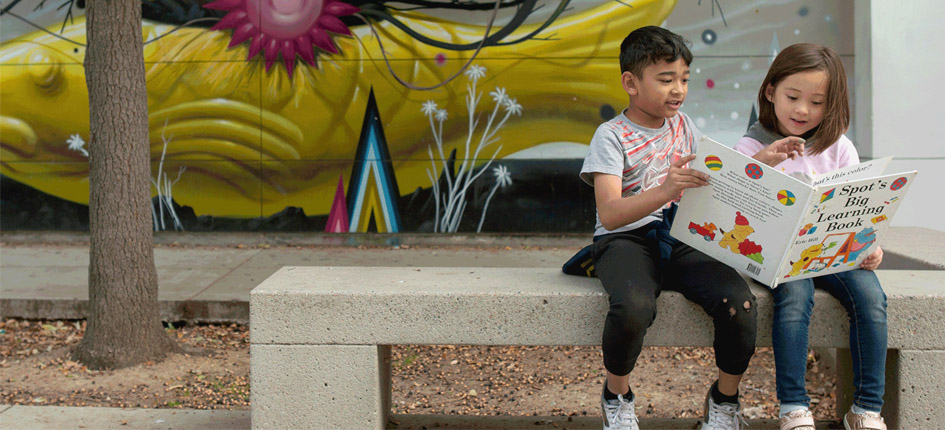 Two children read a book on a bench.