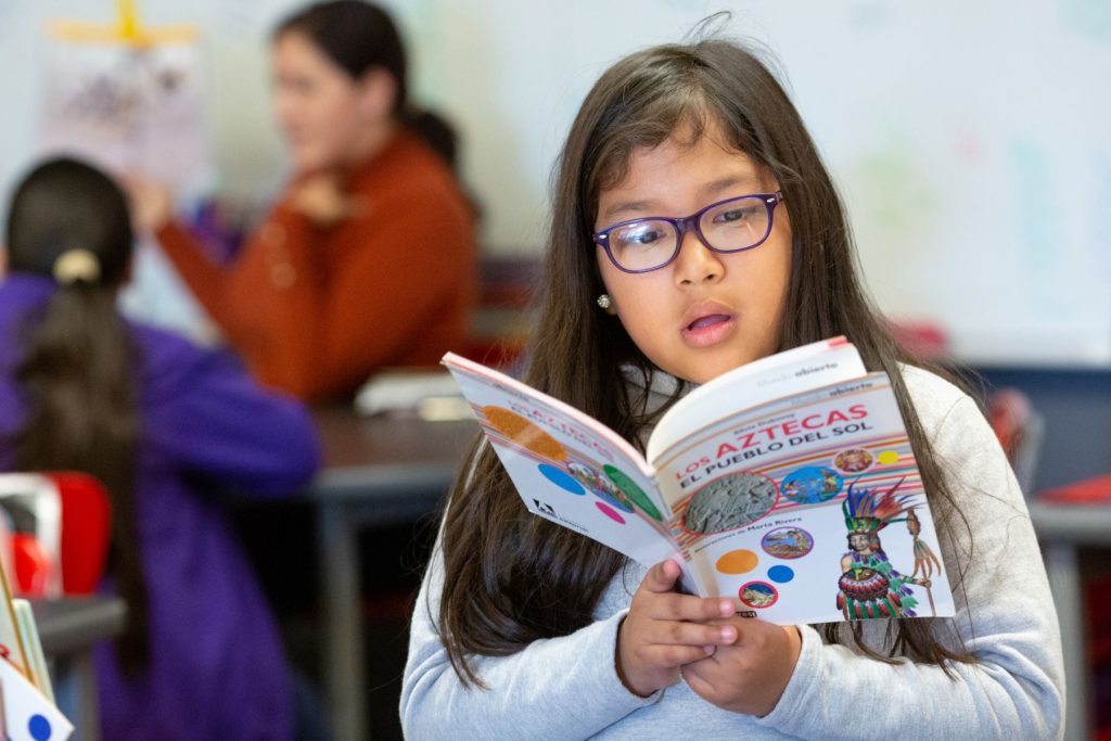 A young girl reading a book in Spanish.